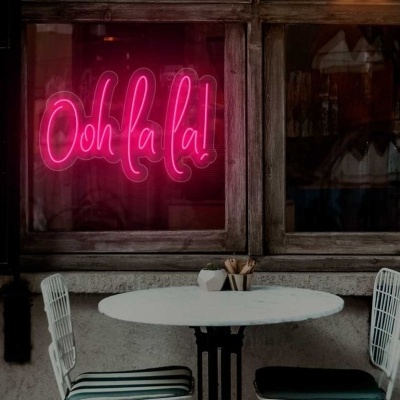 Neon rosa com texto 'Ooh la la!' em janela de madeira, mesa branca redonda e cadeiras brancas com almofadas às riscas verdes