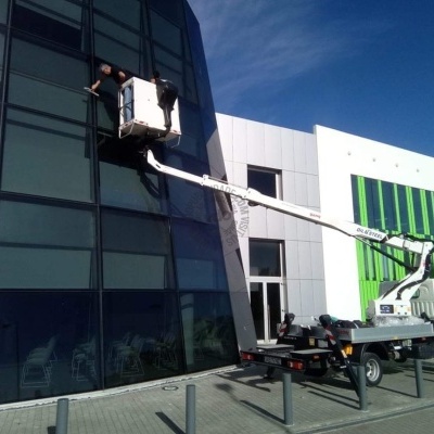 Plataforma elevatória em camião branco junto a edifício moderno com paredes verde, branco e vidro