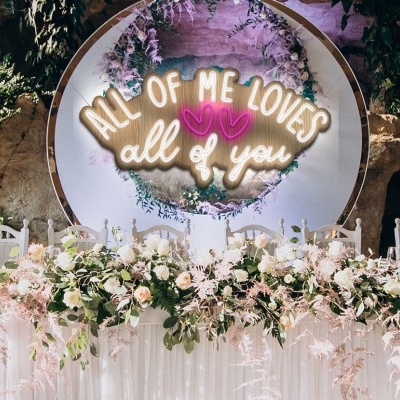 Mesa decorada com flores em arranjo e placa luminosa com texto para evento