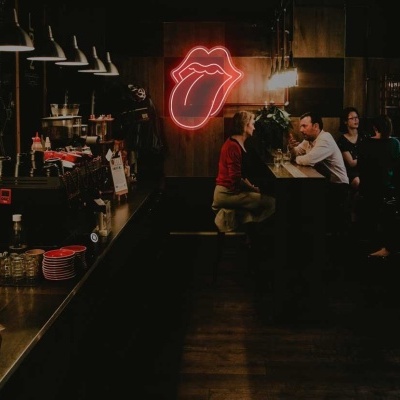Bar escuro com balcão de madeira e neon de língua vermelha na parede