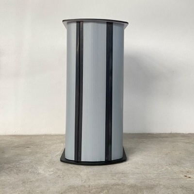 Coluna cilíndrica cinza com faixas pretas em chão de cimento