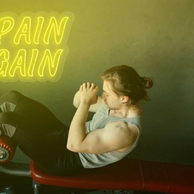 Homem a fazer abdominais num banco de ginásio com texto de néon 'NO PAIN NO GAIN' no fundo
