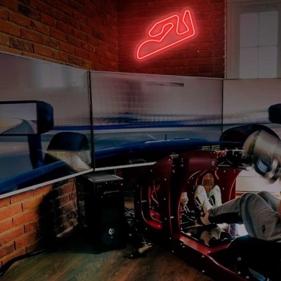 Simulador de condução com volante, pedais e ecrã triplo curvo num ambiente interior com parede de tijolos