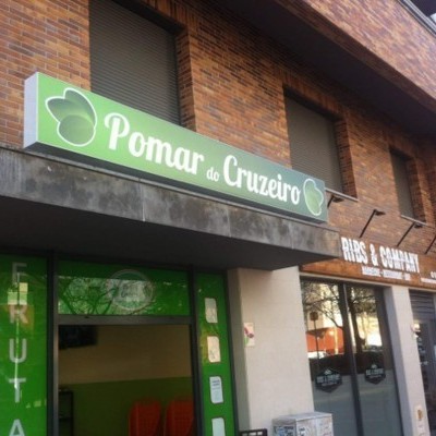 Entrada da loja Pomar de Cruzeiro com placa verde e elementos gráficos de maçãs numa fachada de tijolos.
