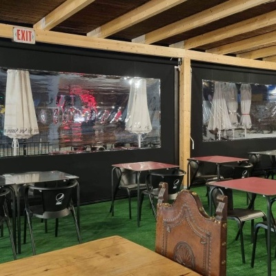 restaurante interior com mesas e cadeiras pretas e vermelhas, carpete verde, teto de madeira e janelas cobertas