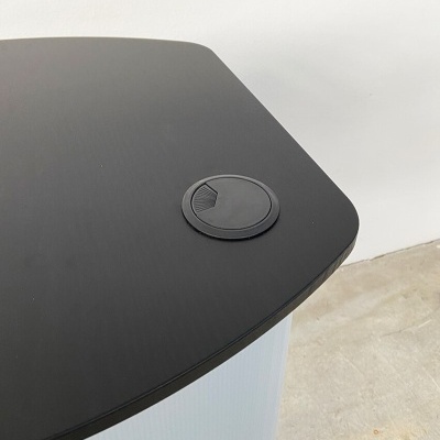 Mesa preta com orifício para cabos em fundo de chão de cimento e parede branca