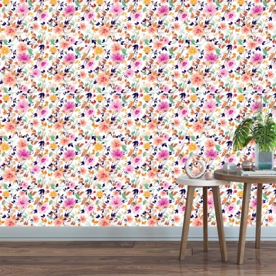 Papel de parede floral colorido numa parede com soalho em madeira escura e duas mesas de madeira clara com objetos