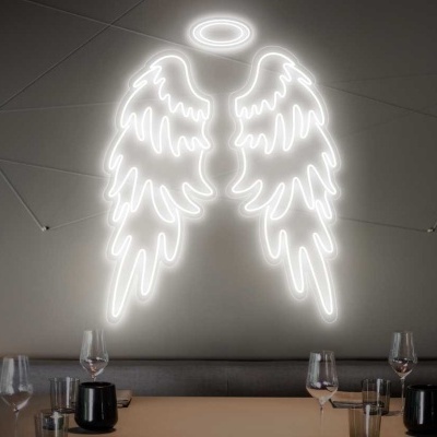 Asas de anjo iluminadas em néon branco numa parede cinzenta com mesa e copos.