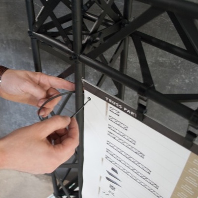 Pessoa a montar estrutura metálica preta com parafuso segurando papel impresso