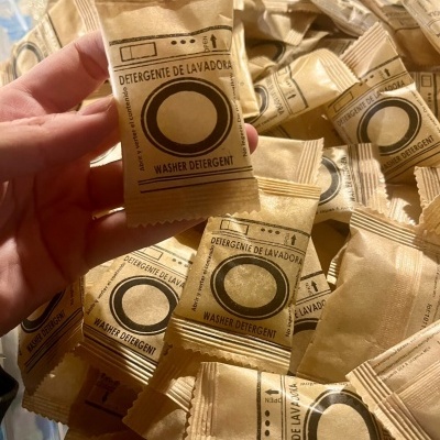 Pacotes individuais de detergente para máquina de lavar em papel castanho com texto e ilustração preta