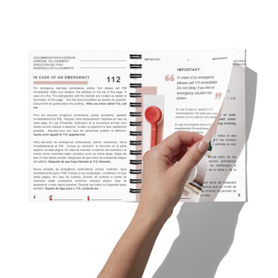 Manual de instruções com informações de emergência, uma mão a virar páginas e um dispositivo vermelho.