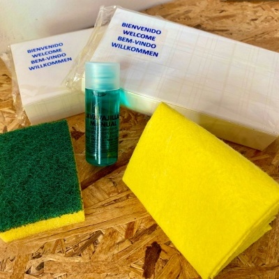 Conjunto de produtos de limpeza com esponja, toalha, frasco azul e pacotes embalados com texto multilíngue