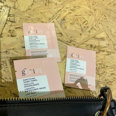 Pacotes rosa e branco de toalhetes higienizantes geeLIFE sobre madeira clara junto a saco preto com fecho