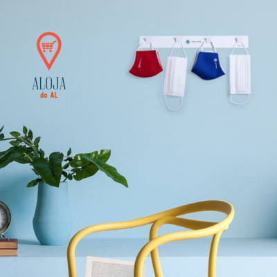 Máscaras comunitárias vermelha, branca e azul penduradas na parede azul clara, vaso azul com plantas, livros, relógio e cadeira amarela à frente