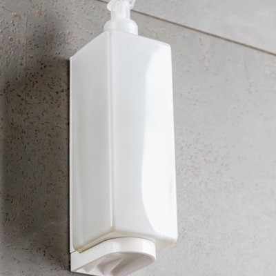 Dispenser de plástico branco com bomba montado numa parede cinza