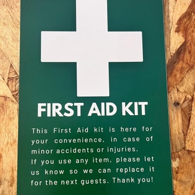 Placa verde com cruz branca e texto FIRST AID KIT sobre madeira clara texturada