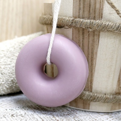 Sabonete rosa em forma de rosquinha pendurado junto a uma toalha e balde de madeira