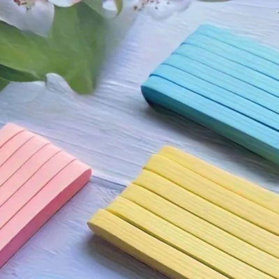 Paus de madeira coloridos em rosa, azul e amarelo organizados em feixes sobre superfície branca