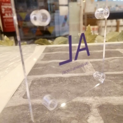 Suporte acrílico transparente com texto roxo invertido sobre superfície cinzenta