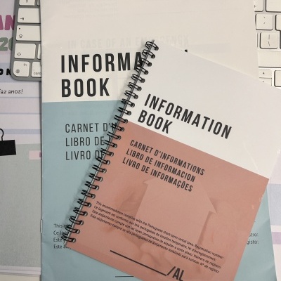 Dois cadernos de informação com capas em branco, azul e rosa sobre um teclado branco.