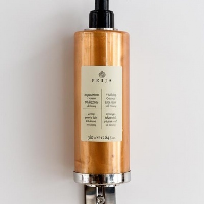 Dispenser dourado de creme vitalizante para banho Prija montado na parede branca
