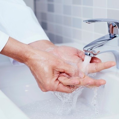 Pessoas lavando as mãos numa pia com azulejos cinzentos
