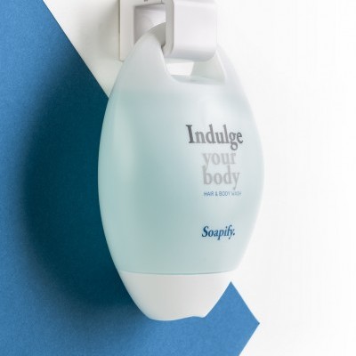 Dispenser de sabonete branco com texto 'Indulge your body' montado numa parede