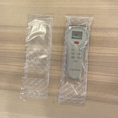 Controlo remoto digital branco com ecrã e vários botões embalado em plástico transparente sobre superfície de madeira