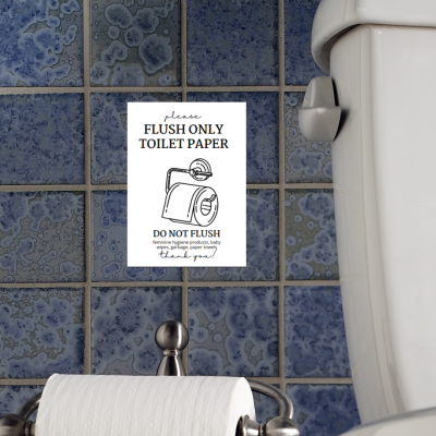 Etiqueta com aviso sobre uso apenas de papel higiénico colada em parede de azulejos azuis, com sanita branca à direita e suporte de papel higiénico à frente.