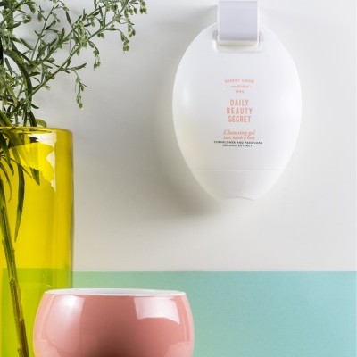 Dispenser de gel de limpeza branco na parede com vaso amarelo e tigela rosa clara