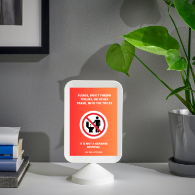 Placa de aviso vermelha em suporte branco sobre mesa com livros e planta verde