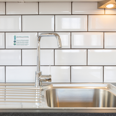 Torneira moderna cromada com lava-louças metálica em cozinha com azulejos brancos