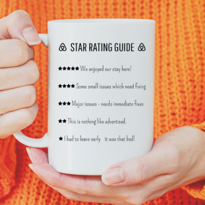 Caneca branca com texto STAR RATING GUIDE e estrelas, segurada por pessoa com camisola laranja.