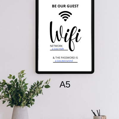 Poster WiFi A5 em moldura preta na parede sobre secretária com planta, livros e canetas