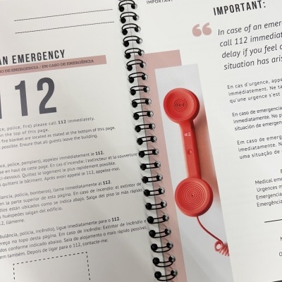 Caderno aberto mostrando informação sobre o número de emergência 112 e uma imagem de telefone vermelho.