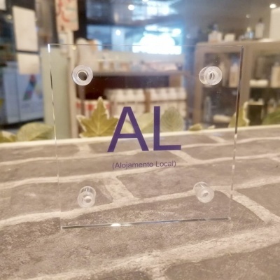 Placa acrílica transparente com texto 'AL (Alojamento Local)' em roxo