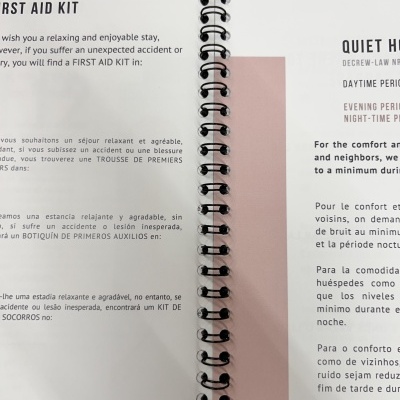 Página impressa com encadernação em espiral e texto multilingue sobre primeiros socorros e silêncio