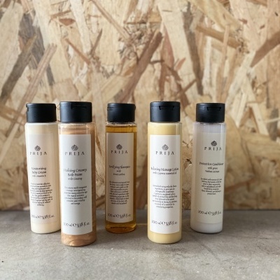 Cinco frascos pequenos de produtos PELIA em plástico com tampas pretas sobre superfície cinza e fundo de madeira clara