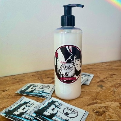 Frasco branco com doseador preto e rótulo 'Lisboa' sobre madeira com pacotes planos ao redor.