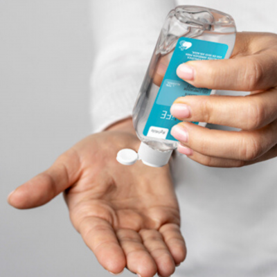 Pessoa a aplicar gel desinfetante para as mãos de frasco com rótulo azul.
