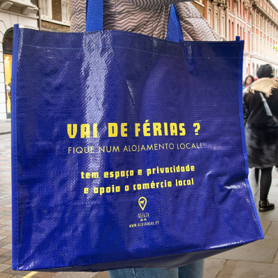 Sacola azul com texto amarelo sobre alojamento local, em rua movimentada