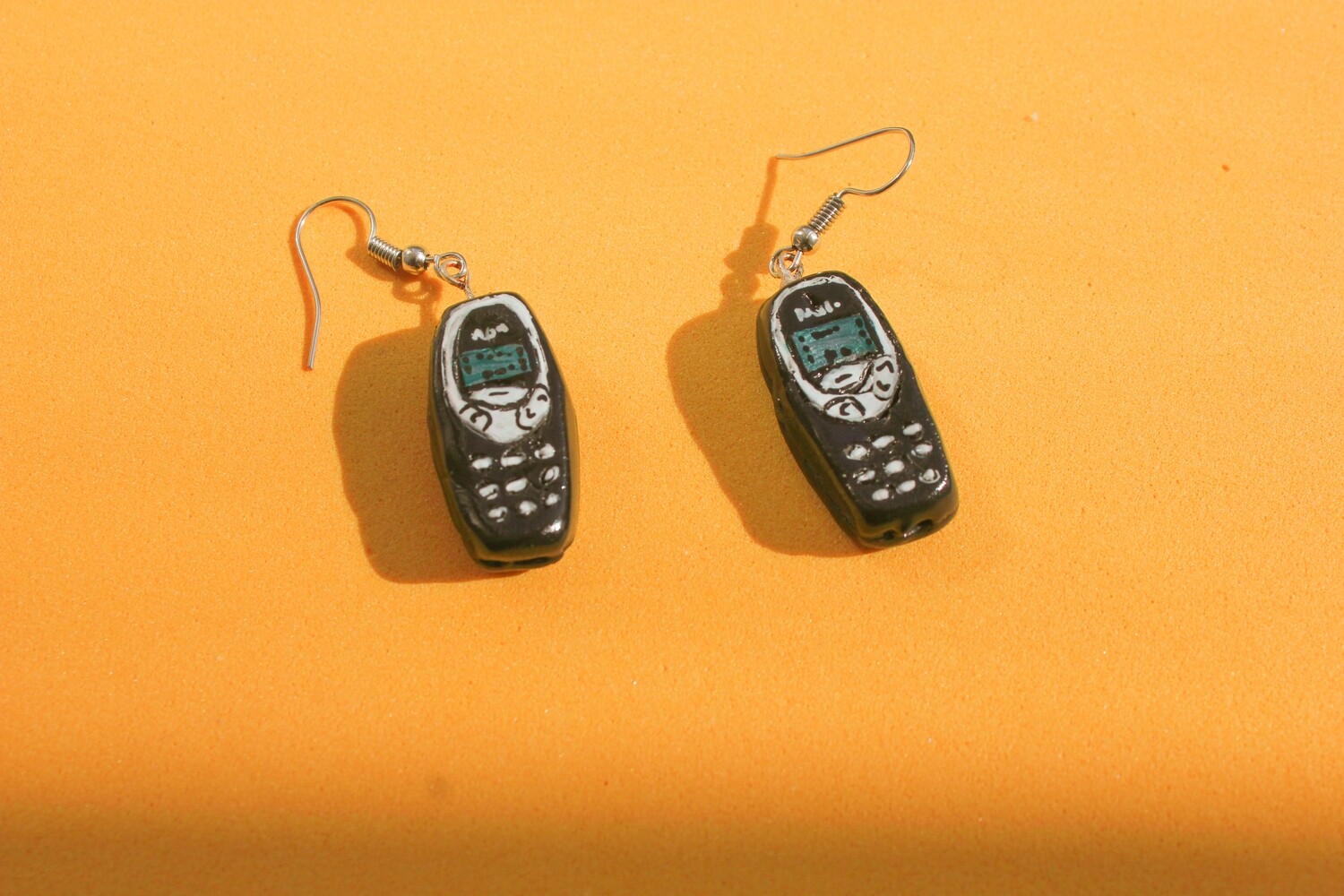 Brincos Nokia Brincos em forma de telemóveis antigos sobre fundo laranja.