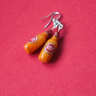 Brincos em forma de garrafas da cerveja Super Bock sobre fundo vermelho.