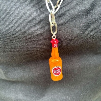 Colar com pendente de garrafa laranja e rótulo SUPER BOCK sobre fundo cinzento