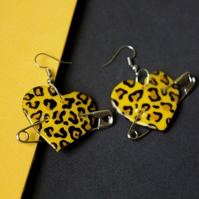 Brincos em forma de coração com padrão de pele de leopardo amarelo e preto e alfinetes de segurança.