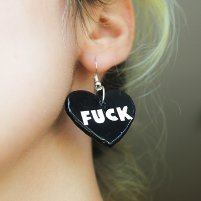 Brinco preto em forma de coração com a palavra FUCK escrita em branco.
