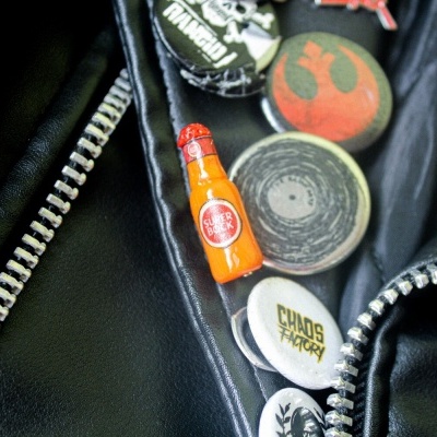 Jaqueta preta com pins coloridos, incluindo garrafa Super Bock e Chaos Factory