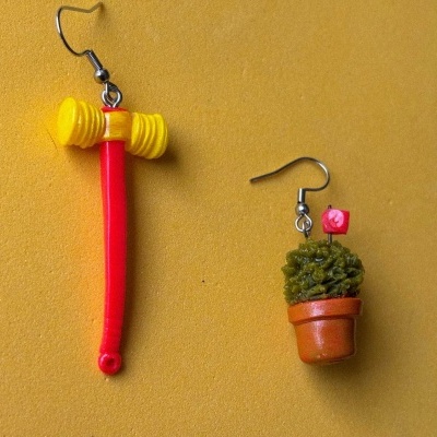 Brincos com formas de martelo e vaso com planta em fundo amarelo.