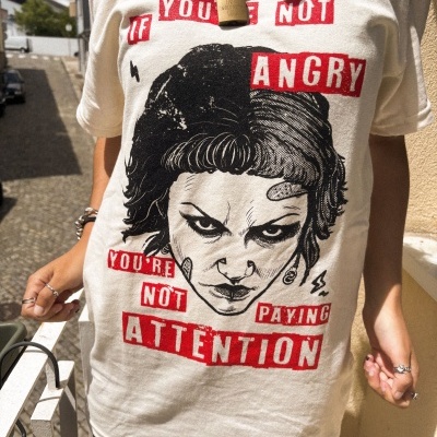 T-shirt bege com estampa de rosto e texto em vermelho e preto com corrente com cadeado.