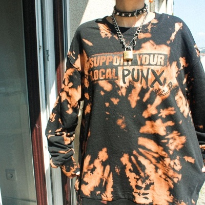 Sweatshirt preta tie-dye laranja com texto e desenho, usada numa varanda